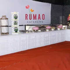 A clean and professional buffet setup featuring our "Rumao Caterers" branding. The white counters and pink chafing dishes can be customized to match your event's color scheme.