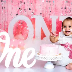 A perfect "look at me" moment. With frosting on her fingers and a huge smile, this is what a successful first birthday cake smash looks like.