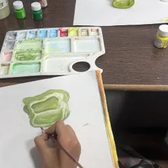 A student works on a detailed painting of a sliced capsicum. Our classes guide students on how to use watercolors to create depth and realism in their still life compositions.