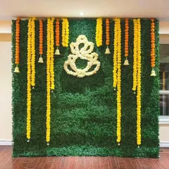 A beautiful and traditional backdrop for a Haldi or Ganesh Pooja ceremony. We use a green grass wall as a base and decorate it with hanging marigold garlands and a Ganesha motif made of white flowers.