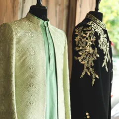 A snapshot from my studio, showing two distinct Indo-Western styles. A mint green jacquard jacket stands next to a black sherwani with bold, gold shoulder embroidery, illustrating the range of my designs.