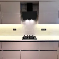A focused shot on the cooking zone, featuring a modern black chimney and hob set against a subtle backsplash. The warm under-cabinet lighting provides excellent task illumination while enhancing the kitchen's sophisticated ambiance.