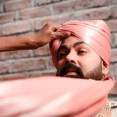 A candid moment of the groom getting ready. This photo captures the tying of the safa or turban, a significant ritual that is part of the groom's wedding preparations.
