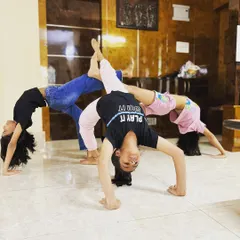 A creative group pose where three young students form a connected bridge. This demonstrates the strength, flexibility, and coordination they develop through consistent practice.