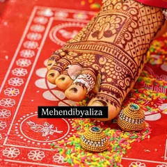 A close-up of a bride's feet with a rich, dark henna stain. The color is absolutely perfect against the red alta.