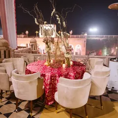 An elegant outdoor seating arrangement for a welcome dinner in Agra. The table is set with a beautiful patterned tablecloth and floral centerpieces, overlooking the venue's stunning architecture.