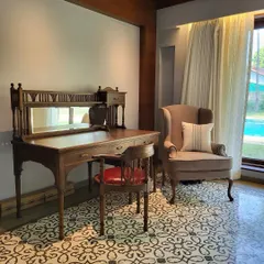A quiet study corner in the Alibaug villa, featuring our custom upholstery on a classic wingback chair. The neutral fabric and simple cushion complement the vintage-style wooden desk and patterned floor tiles.