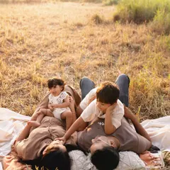 A quiet moment during a family picnic. The whole family lies together on a blanket, enjoying the golden hour light and each other's company.