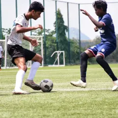 A young footballer skillfully shields the ball from a defender during a practice match. These game simulations are crucial for developing tactical awareness and on-field decision-making.
