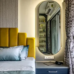 A close-up of a bedroom design showing a custom bedside table integrated with a vibrant yellow upholstered headboard. The backlit full-length mirror adds depth and functionality to the space.