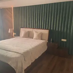 This bedroom features a stunning contrast of textures. A custom-made, deep green fabric wall paneling creates a dramatic backdrop for the bed, which is flanked by bookmatched veneer panels for a touch of natural elegance.