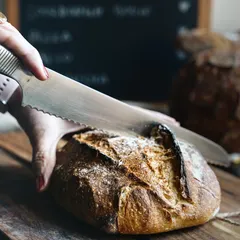 The satisfying moment of slicing into a freshly baked sourdough loaf, capturing the texture of the crust and the promise of the soft crumb inside.