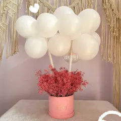 Simple elegance. This beautiful arrangement features a cloud of white balloons floating above a box of delicate pink dried flowers, making for a chic and modern gift.