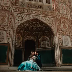 A couple shares a laugh while seated in an ornate archway, with intricate floral patterns creating a rich, textured background. This shot showcases the vibrant colors and detailed architecture of Rajasthani palaces.
