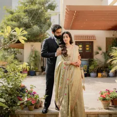 An engagement portrait that exudes grace and sophistication. The groom gently holds his bride, both dressed in elegant attire, surrounded by the lush greenery of a beautiful home garden.
