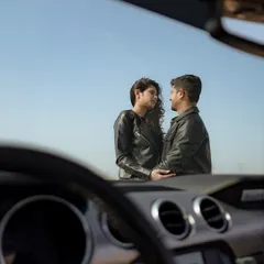 An artistic shot from inside the car, framing the couple against the vast desert sky, creating a sense of intimacy and adventure.
