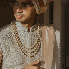 A classic, elegant portrait of a groom in his sherwani and pearl necklace, with soft window light highlighting his features.