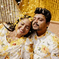 A close-up of the couple covered in turmeric and flower petals, sharing a quiet, happy moment amidst the chaos. It's a beautiful, intimate shot.