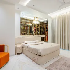 This angle showcases the elegant chandelier and the spacious layout of the bedroom. The vibrant orange armchair adds a pop of color, creating a cozy reading corner.