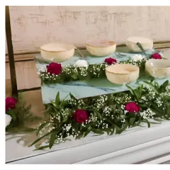 A dessert station featuring individual portions served in elegant bowls. The display is tiered and decorated with fresh red roses and baby's breath for a romantic touch.