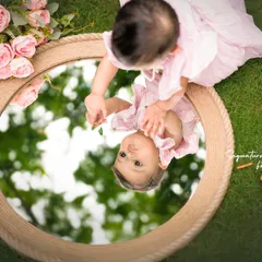 A creative perspective from an outdoor shoot, capturing the baby's reflection as she looks into a rustic mirror on the grass.