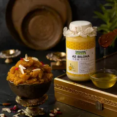 A festive shot featuring a bowl of Moong Dal Halwa, with golden ghee being drizzled on top. The traditional brassware and rich, warm tones evoke a sense of celebration and indulgence.