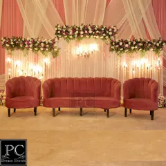 I designed this elegant engagement stage with a dusty rose velvet sofa set, a backdrop of white drapes, and delicate floral arrangements with hanging lights for a soft, romantic glow.