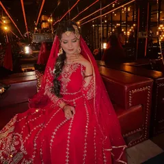 Captured in a warm, ambient setting, this photo highlights the rich red tones of the Pakistani bridal attire. The makeup remains flawless under the lights, showcasing a radiant complexion and beautifully defined features.
