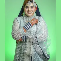 A bright, joyful portrait of a bride during her Nikah ceremony. Her beautiful smile is the centerpiece, captured against a clean, vibrant green background to make her silver and blue attire stand out.