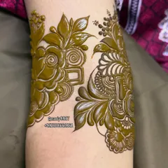 A close-up of a floral motif being created on the arm. The raised paste shows the precision of the application.