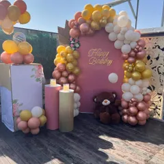 A beautiful terrace birthday decoration with a warm, earthy color palette. The setup includes a pink backdrop and a balloon arch in gold, white, and rose gold, perfect for a daytime or sunset party.