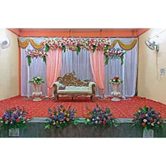 This is our classic stage decoration for a formal event like a reception or engagement. The setup includes a beautiful floral valance, elegant pink and white drapes, a regal lounge sofa, and matching flower arrangements on urns.