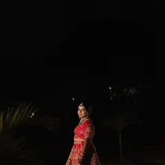 A dramatic bridal portrait under the night sky. The bride in her red lehenga stands out against the darkness, with a crescent moon above, creating a magical and powerful image.