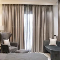 This luxury bedroom showcases a comfortable grey chaise lounge and armchair, perfect for unwinding. The floor-to-ceiling curtains add a touch of drama and softness to the room.