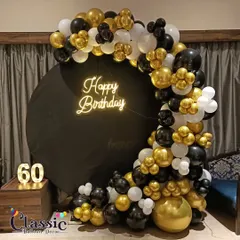 For milestone birthdays like a 60th, we design elegant setups. This one features a black and gold balloon semi-arch on a circular backdrop with a custom neon sign and marquee numbers.