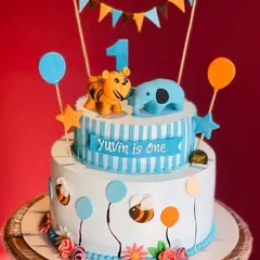 A cheerful two-tier cake for Yuvin's first birthday. This design includes cute animal toppers, balloons, and a festive banner, perfect for a little one's milestone celebration.