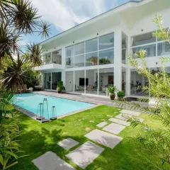 This modern villa features floor-to-ceiling windows that look out onto a tropical paradise. I used a combination of lush lawns, stone pavers, and mature palm trees to create a luxurious, resort-like feel right at home.