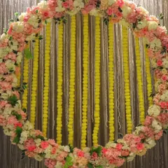 A beautiful circular backdrop made of pink and white flowers with strings of yellow marigolds. This versatile design is perfect for a Haldi, Mehandi, or Sangeet photo booth.