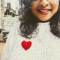 A selfie showing off one of my small, bright red crochet hearts pinned to my sweater. It's a cute little accessory that adds a pop of color and love to any outfit.