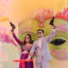 A vibrant and energetic shot from a carnival-themed pre-wedding event. The couple makes a grand entrance with color smoke guns, perfectly capturing the fun and celebratory spirit of the day.