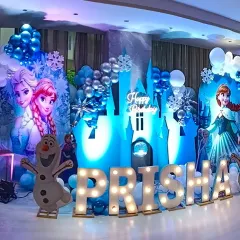 Bringing the magic of Arendelle to life with a complete Frozen theme party setup. This includes character cutouts of Elsa, Anna, and Olaf, an illuminated ice castle backdrop, snowflake details, and a balloon garland in signature icy blue, white, and silver tones. The light-up marquee letters for the name make it extra special.