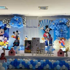 An elaborate Mickey Mouse themed birthday party stage, filled with blue and white balloons, character cutouts, and personalized backdrops.