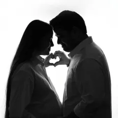 A classic silhouette of the couple, their profiles outlined against a bright white background. The partner forms a heart with his hands over the baby bump, a simple yet profound gesture of love.