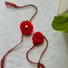 Two of my handmade rakhis in a beautiful, vibrant red. One is a pom-pom flower with a pearl, and the other is a delicate knitted rose. They are a special way to share a bond.
