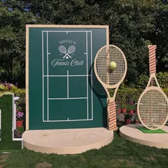 A sophisticated Tennis Club theme for a first birthday. The main photo backdrop features a custom tennis court design, oversized rackets, and a grass-covered number '1'.