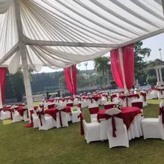 This image shows a classic banquet seating arrangement on a lawn, perfect for a wedding lunch. The tables are dressed in red and white linen, matching the drapes of the tent structure.