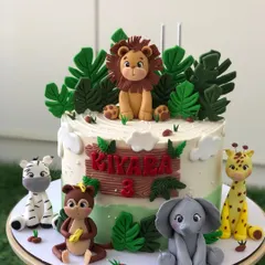 A cute jungle-themed cake for a third birthday, surrounded by handcrafted fondant animals like a lion, elephant, zebra, and monkey.