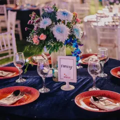 A vibrant table setting with a rich blue velvet tablecloth and contrasting red plates. The colorful floral centerpiece and custom "Family" table sign add a personal and lively touch.