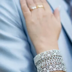 A close-up detail shot of the wife's hand, adorned with beautiful diamond bracelets and her wedding ring, resting on her husband's suit.
