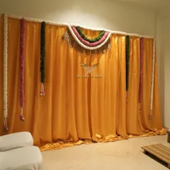A simple and traditional pooja backdrop for a house warming, using a bright yellow fabric and classic floral thorans.